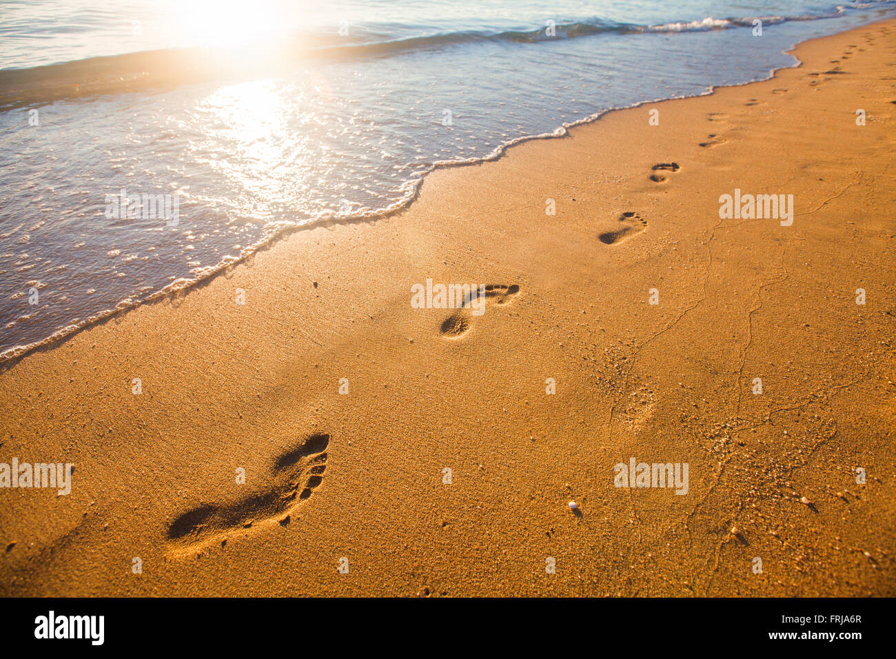 Spiaggia, onde e impronte in tempo al tramonto Foto Stock