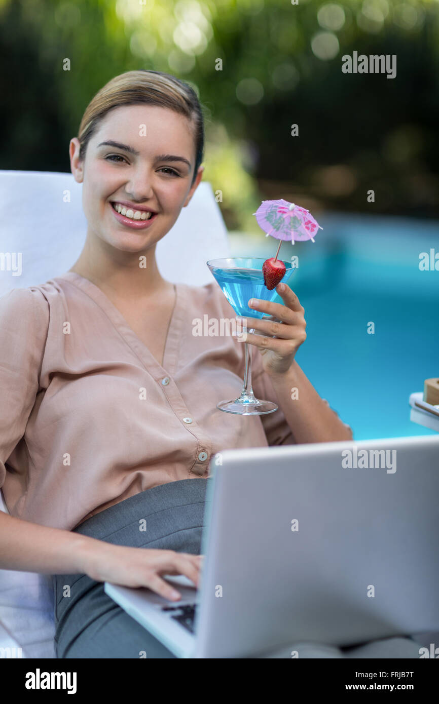 Imprenditrice tenendo un bicchiere di martini durante l'utilizzo di laptop Foto Stock