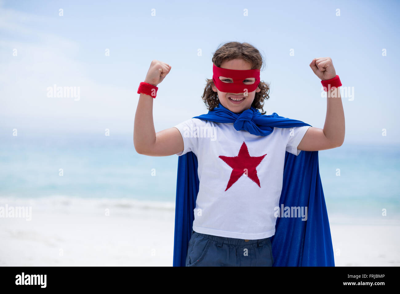 Ragazzo in costume da supereroe pugno di aggraffaggio a beach Foto Stock