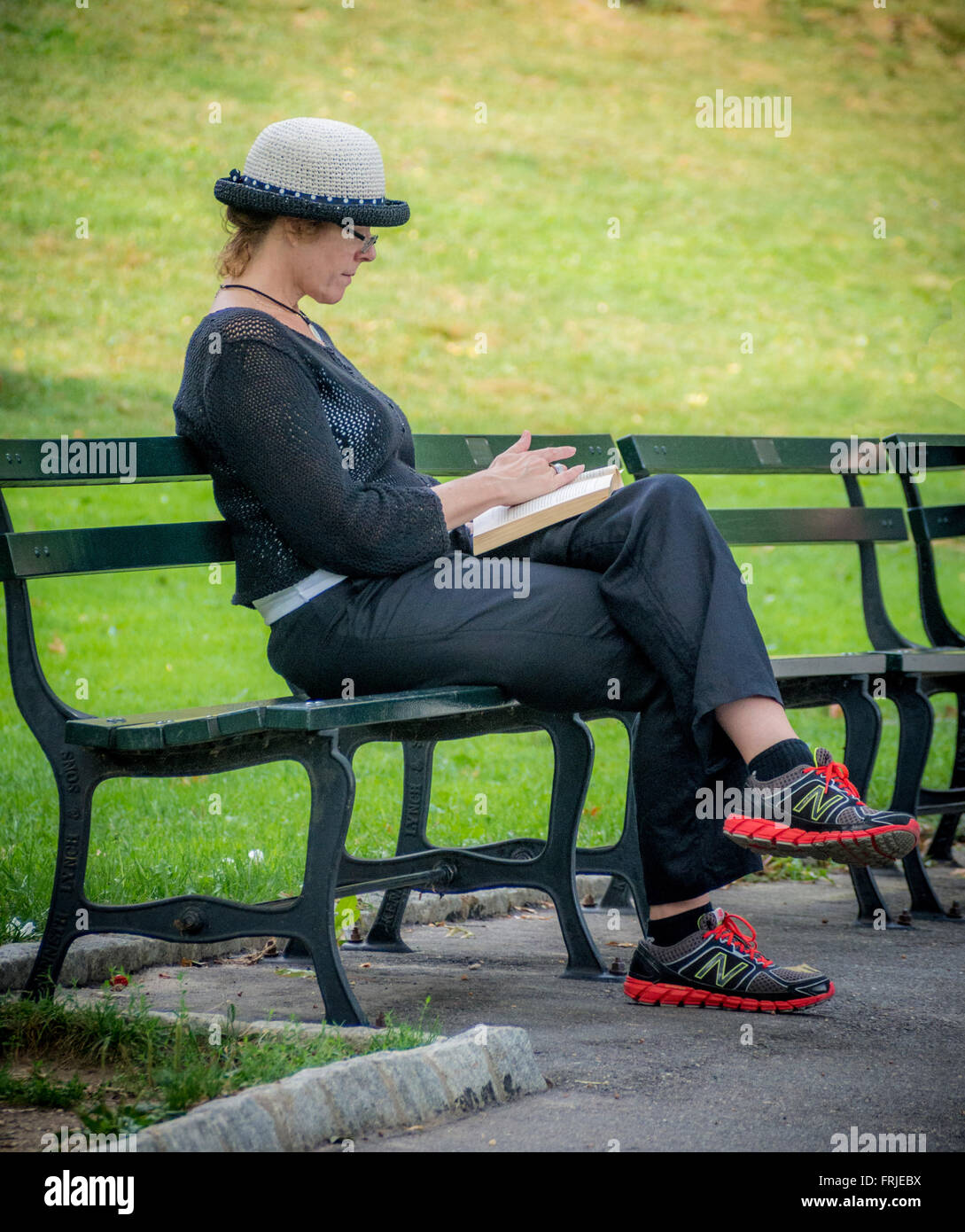 Donna seduta su banco del libro di lettura nel Central Park di New York City, Stati Uniti d'America. Foto Stock