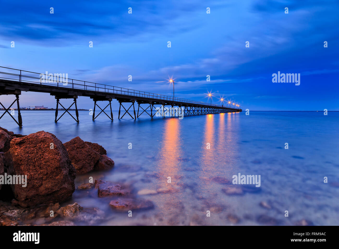 Basso punto di vista lungo pontile in legno e rocce costiere in Ceduna town bay quando acqua trasparente mostra fondali bassi di sunrise. Foto Stock