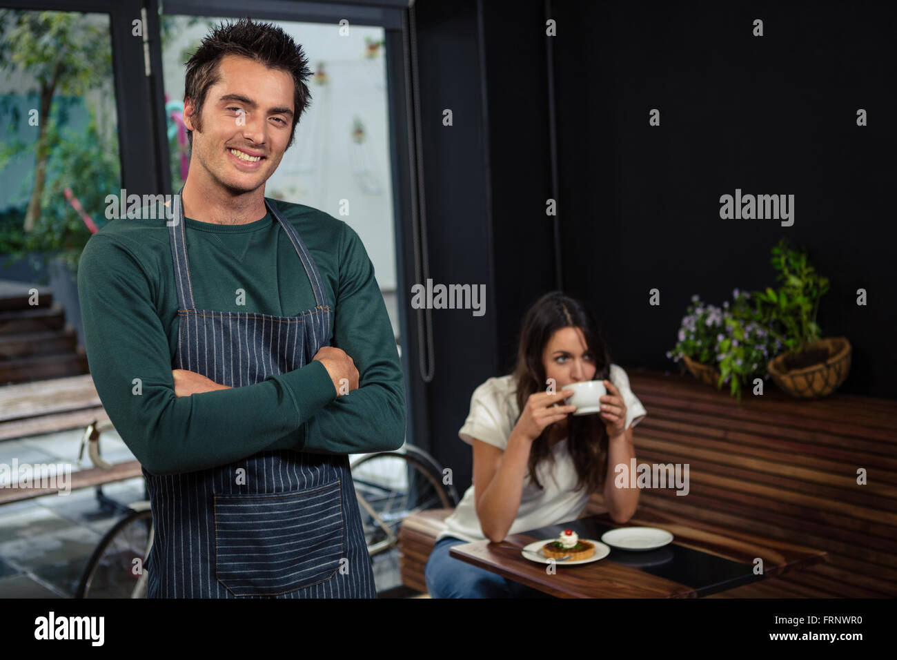 Cameriere sorridente in posa con bracci croce davanti di client Foto Stock