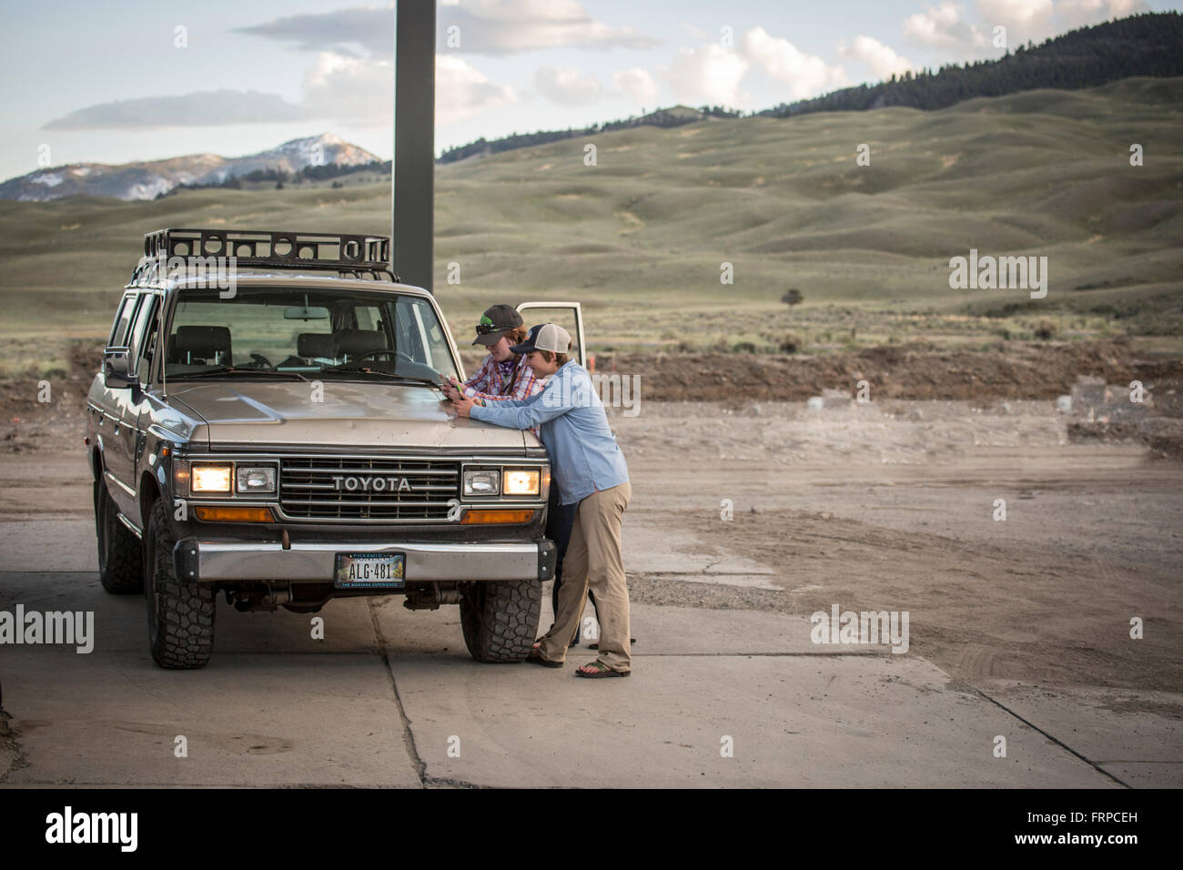 Due ragazze testo sui loro telefoni mentre in corrispondenza di una zona rurale montana stazione di gas con un 1990 Toyota Land Cruiser. Foto Stock