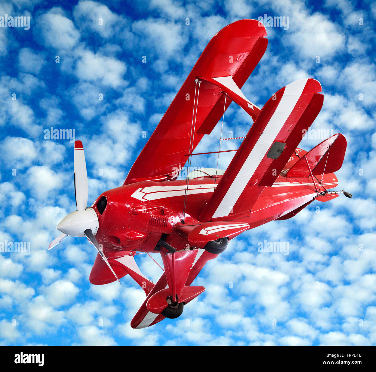 Rosso modello biplano vintage battenti midair e banking contro un nuvoloso cielo blu Foto Stock