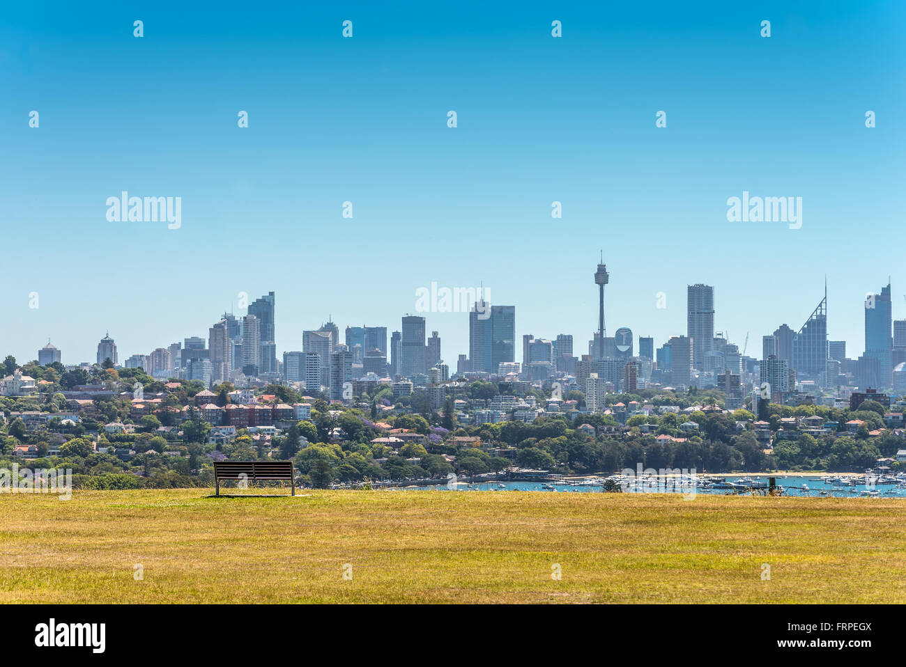 La vista di Sydney dello skyline della città in una leggera foschia. Panca su un prato verde in primo piano Foto Stock
