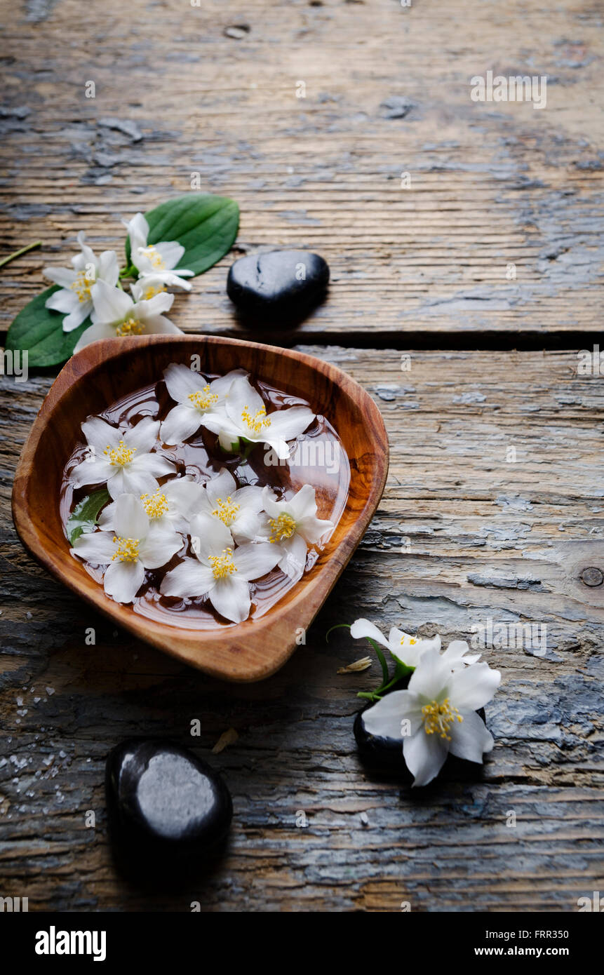 Spa concept. jasmin fiore e spa pietre sul tavolo di legno. Foto Stock