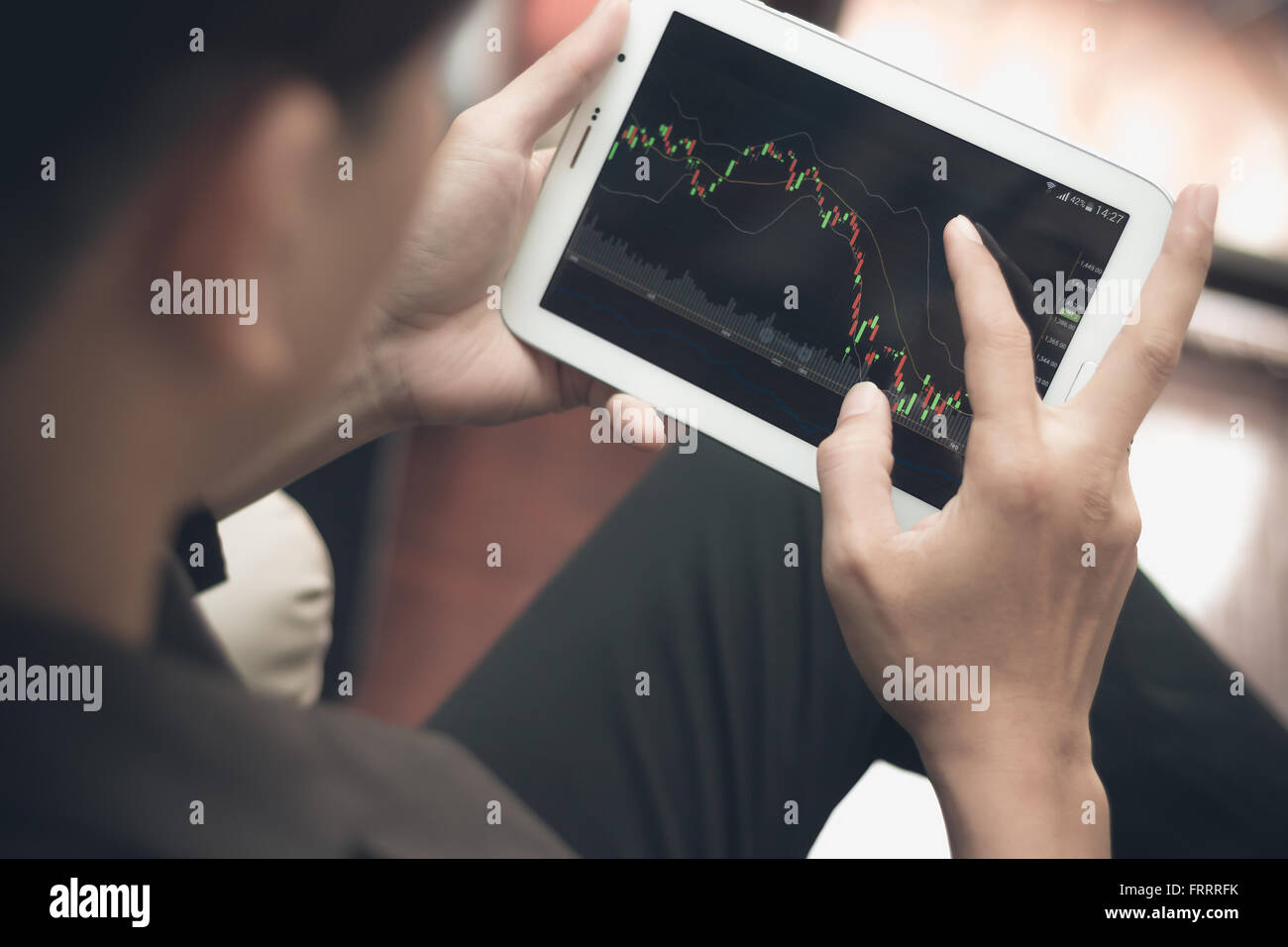 Un uomo di controllare il mercato azionario su tablet e smartphone Foto Stock