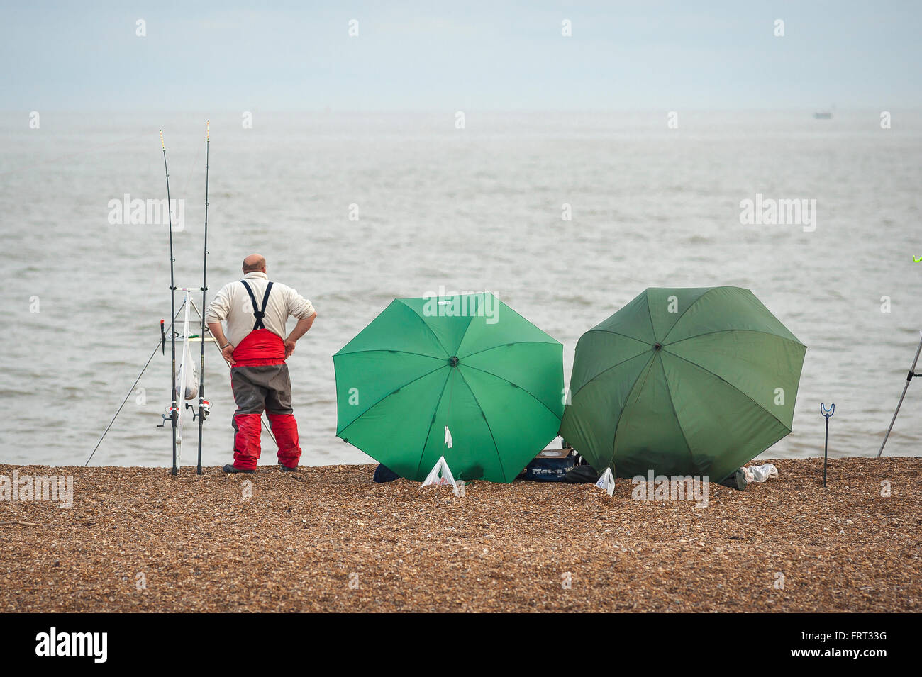 L'uomo la pesca da sola spiaggia, un pescatore attende pazientemente sulla spiaggia di ciottoli vicino Hollesley, Suffolk, Inghilterra. Foto Stock