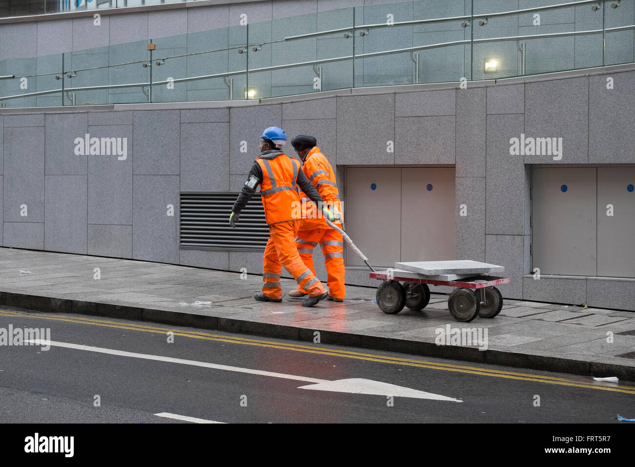 Due lavoratori edili tirando un carrello portante pavimentazioni nel centro della città di Birmingham, Inghilterra, Regno Unito Foto Stock