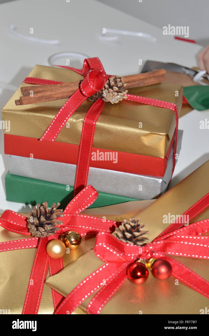 Pile di doni confezionati e pronti per il Natale. Oro Argento rosso e verde confezione regalo con nastri rossi baubles coni fir cannella Foto Stock