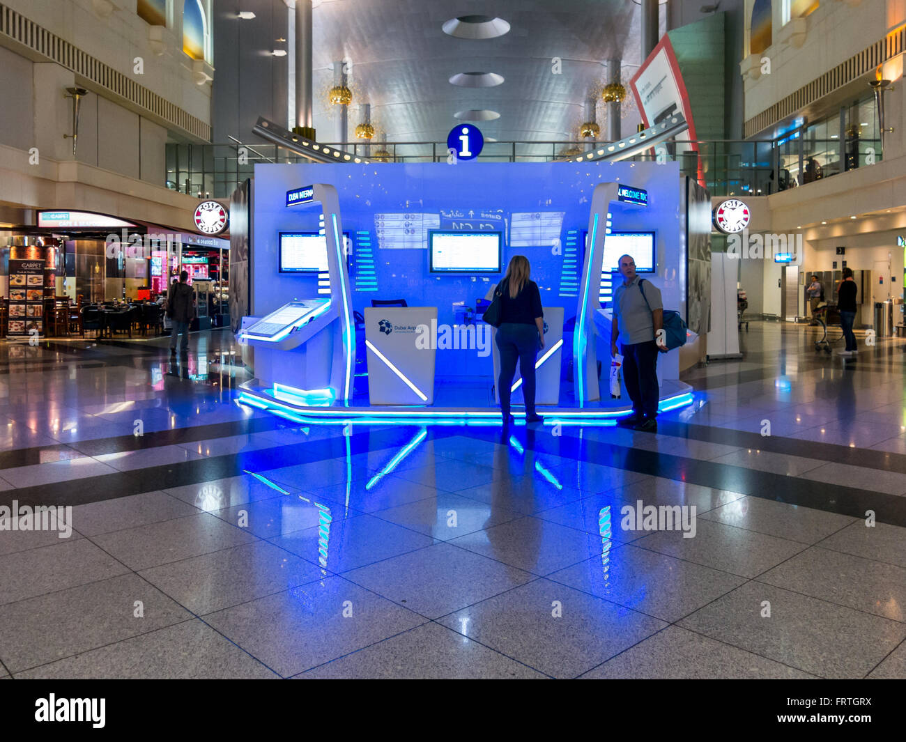 I passeggeri in cerca di informazioni sul viaggio nella sala del terminal dell'Aeroporto Internazionale di Dubai, Emirati Arabi Uniti Foto Stock