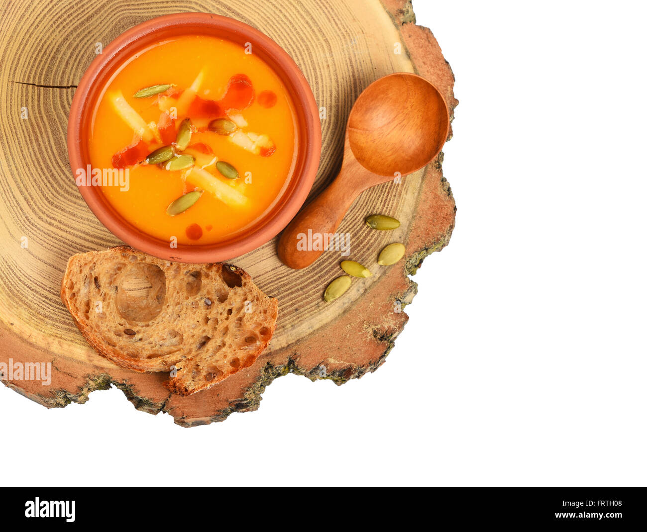 Piccolo vaso in ceramica di crema di zucca zuppa, il cucchiaio di legno, fetta di pane e semi sul taglio di legno isolato su sfondo bianco, top v Foto Stock