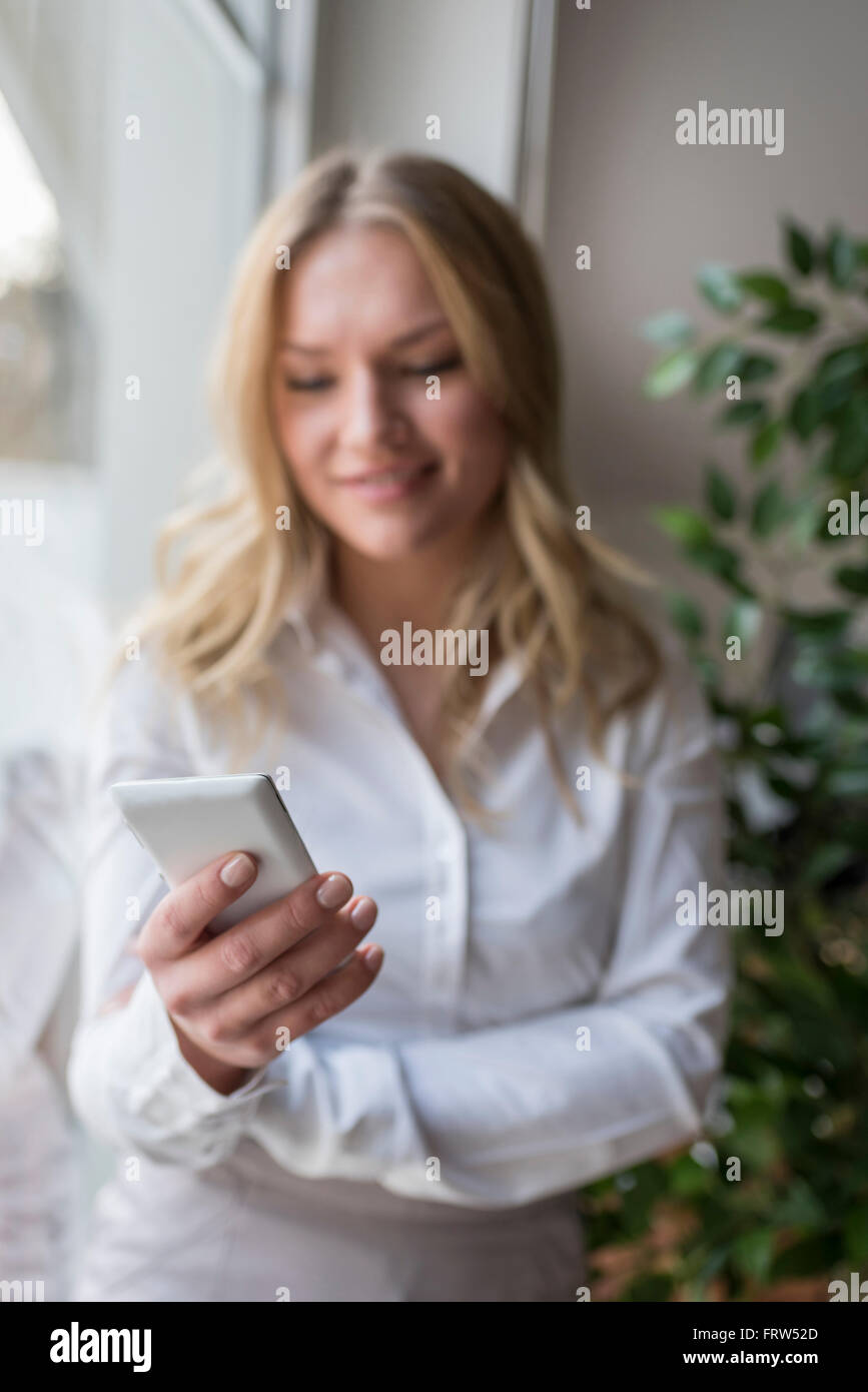 Giovane donna azienda telefono cellulare in corrispondenza della finestra Foto Stock