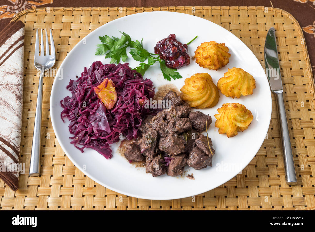Il cinghiale gulasch con cavolo rosso, crocchetta, lingonberry e prezzemolo su piastra Foto Stock