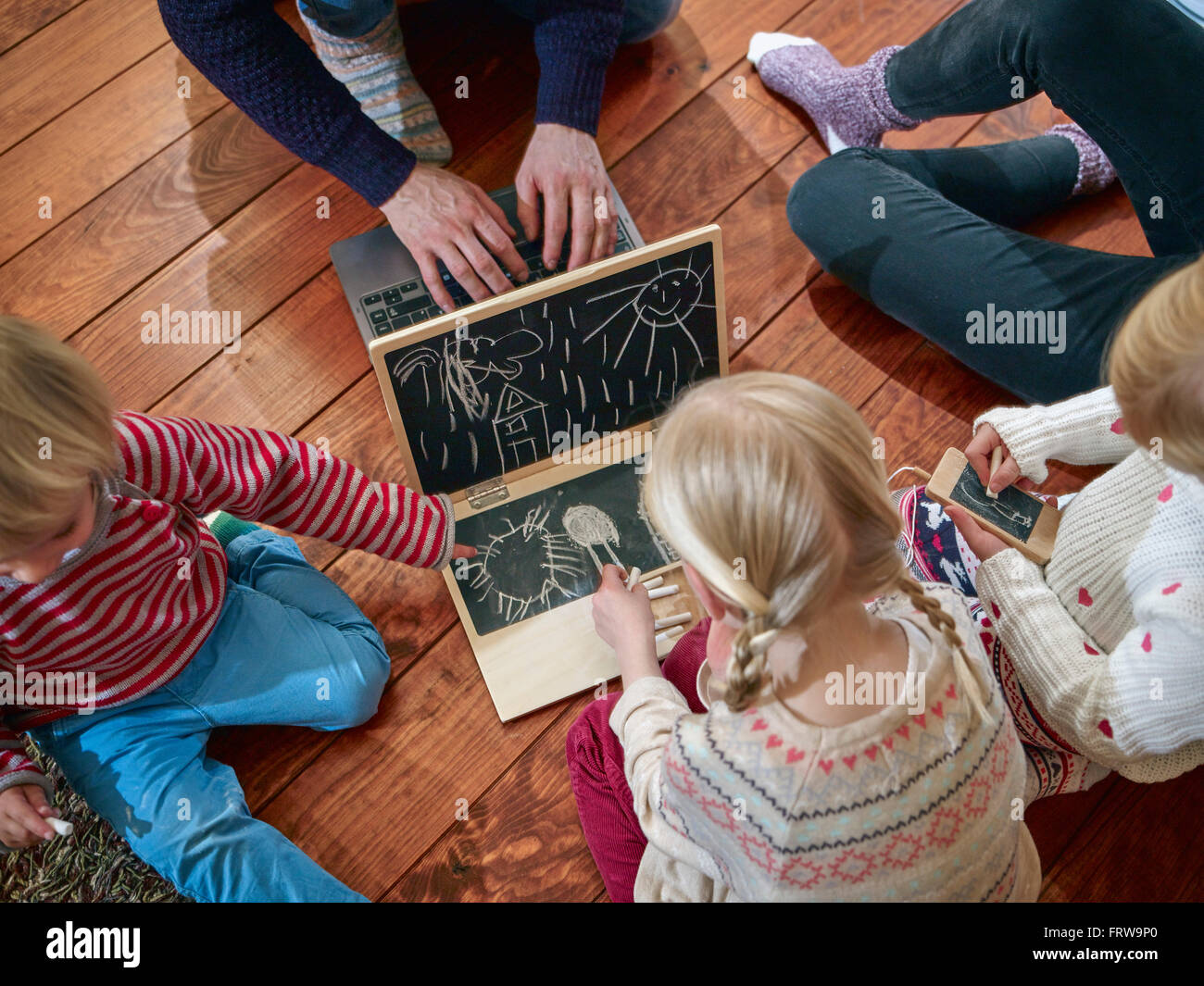 Padre utilizzando laptop seduto sul pavimento con le figlie disegno sul giocattolo di laptop Foto Stock