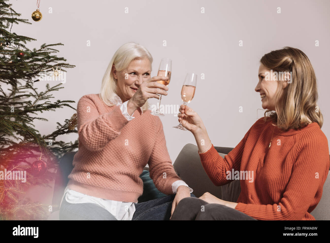 Senior e la donna più giovane donna tintinnanti bicchieri da albero di Natale Foto Stock