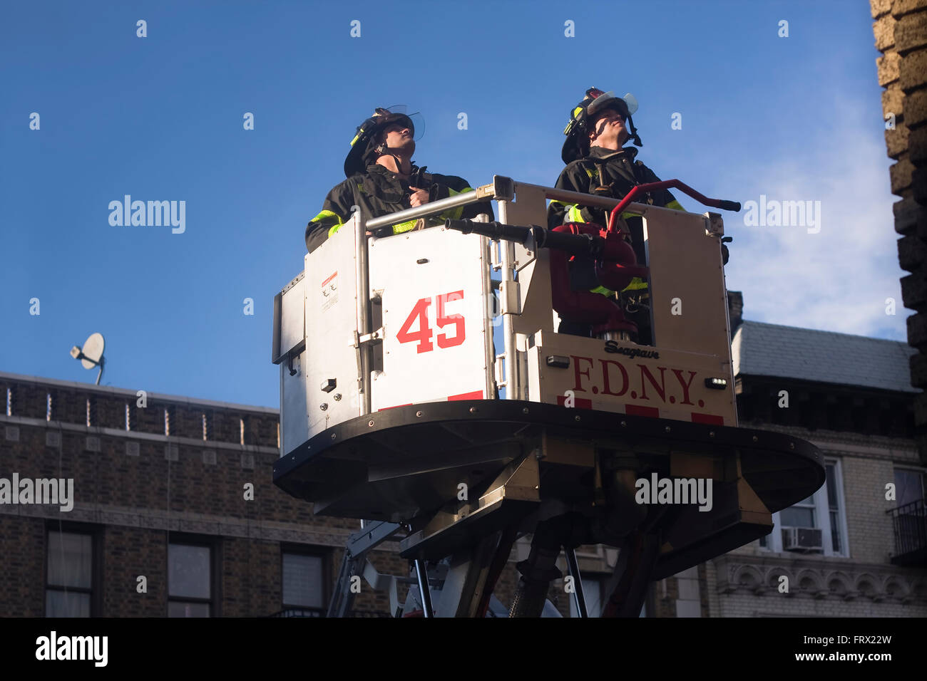 Due vigili del fuoco dal motore 45 in Manhattan sollevato all'interno di una piattaforma aerea scala camion della benna per il lato di un edificio Foto Stock