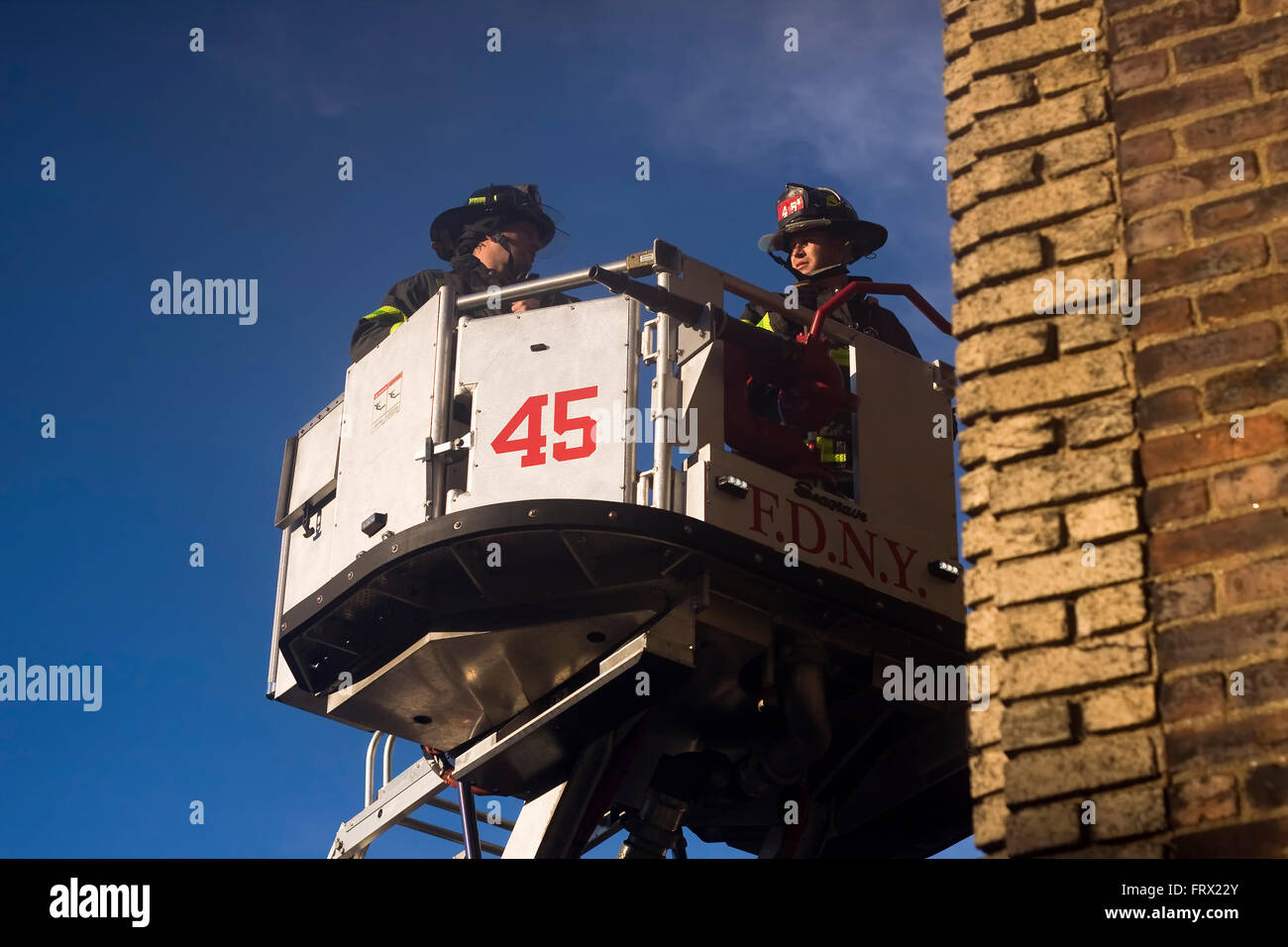 Due vigili del fuoco dal motore 45 in Manhattan sollevato all'interno di una piattaforma aerea scala camion della benna per il lato di un edificio Foto Stock