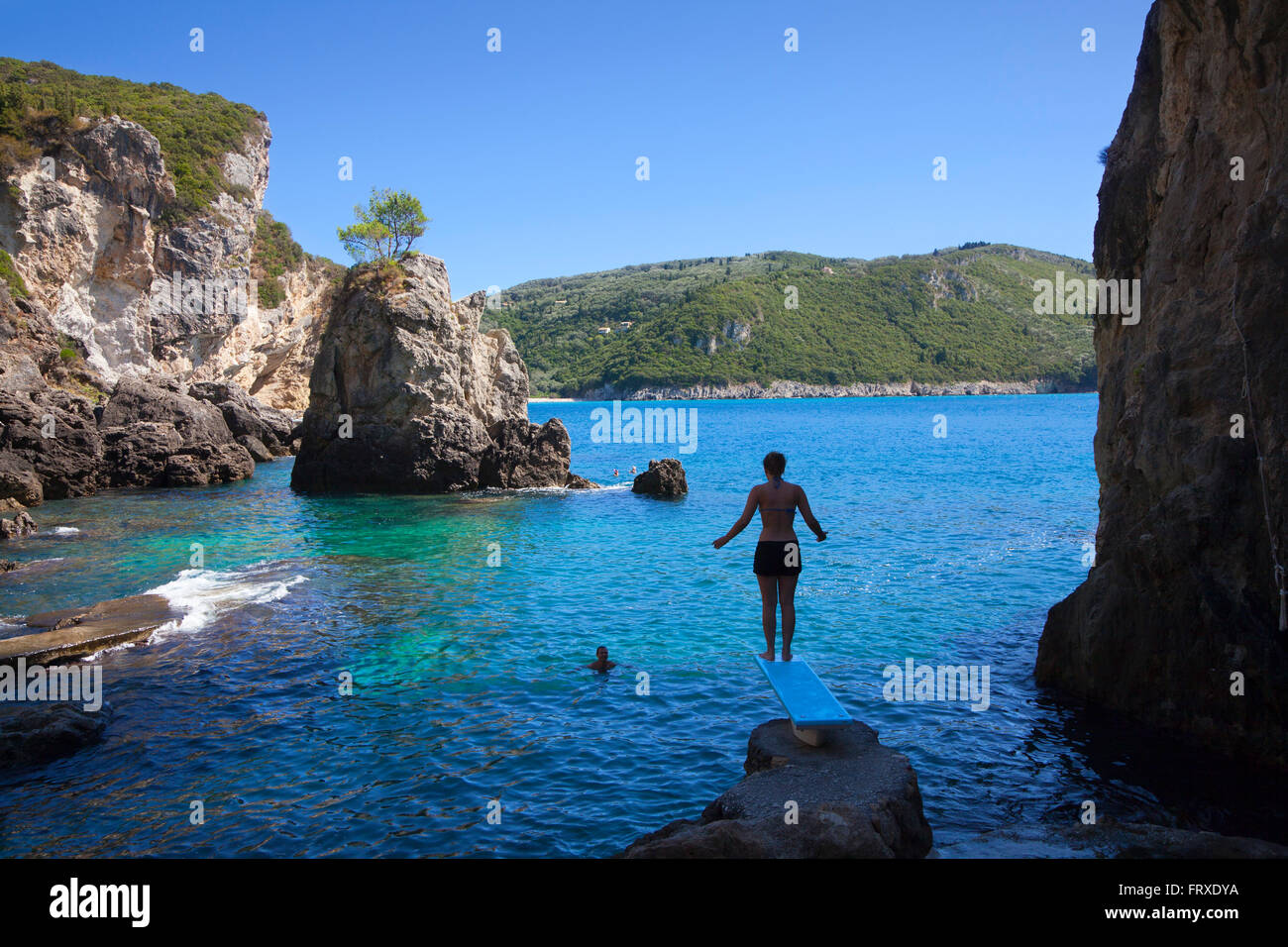 Donna su un trampolino vicino la spiaggia e il bar La Grotta, La Grotta Bay, vicino a Paleokastritsa, isola di Corfu, isole Ionie, Grecia Foto Stock