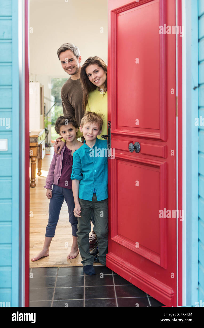 Un bel nucleo familiare di quattro persone è di aprire il loro elegante  porta rossa per accogliere gli ospiti. I genitori e i loro due bambini sono  sorridente e di indossare un