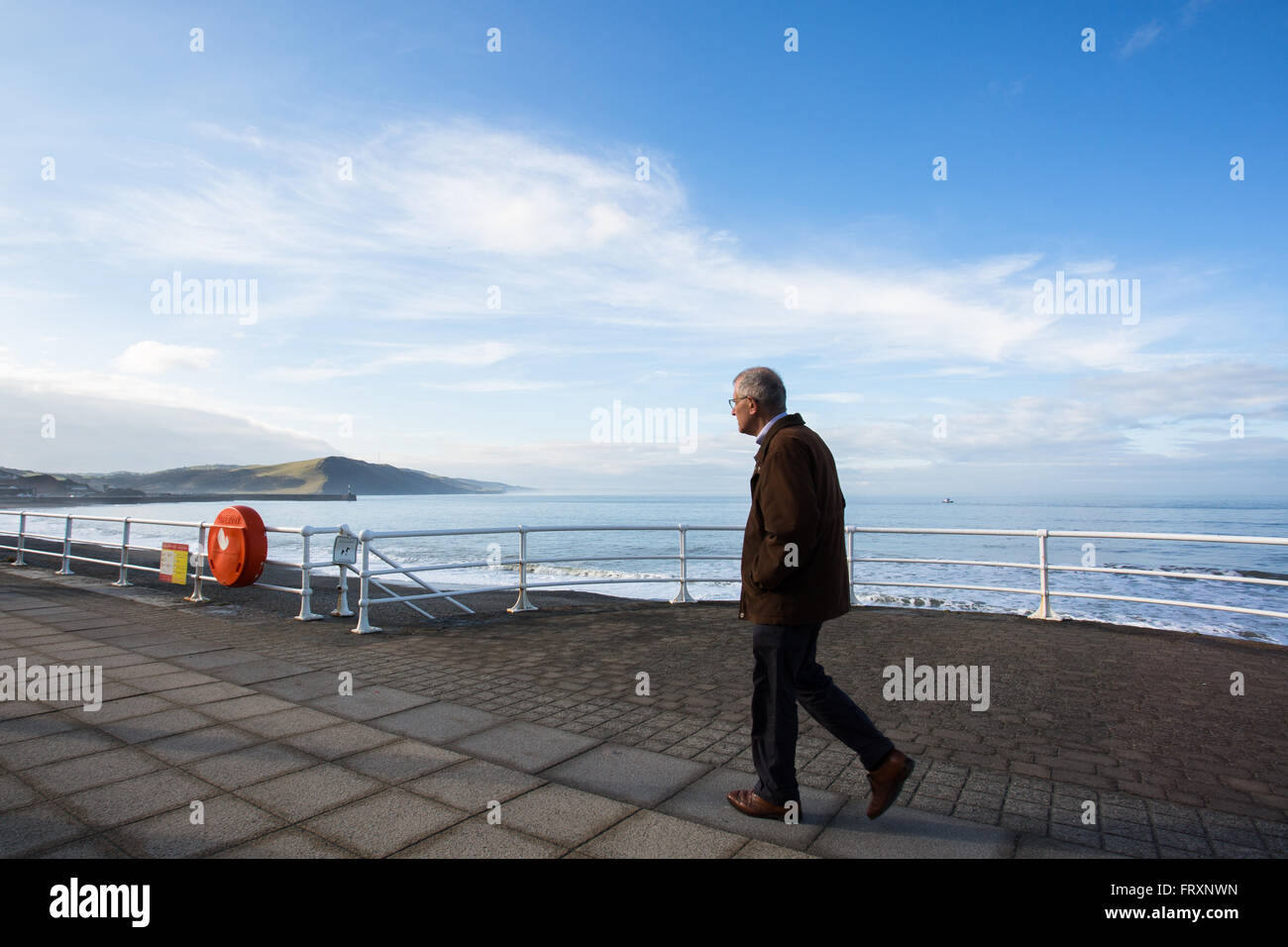 Un elegantemente vestito uomo a camminare lungo Aberystwyth promenade su un chiaro luminoso giorno Foto Stock