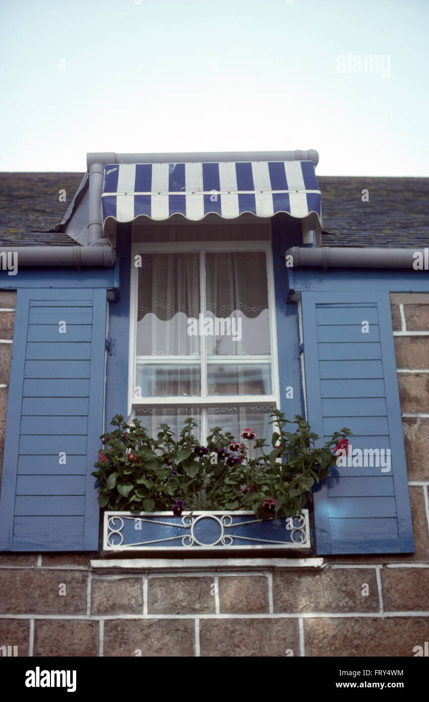 Esterno della piccola casa con tenda a strisce sulla finestra con persiane blu Foto Stock