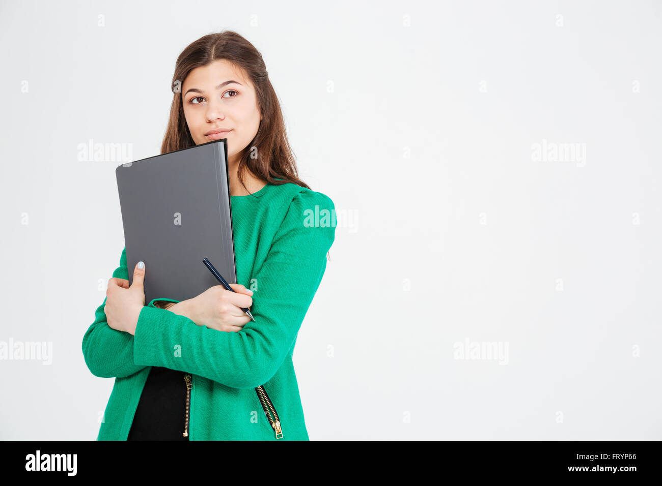 Considerato attraente giovane donna in giacca verde azienda cartelle e riflettendo su sfondo bianco Foto Stock