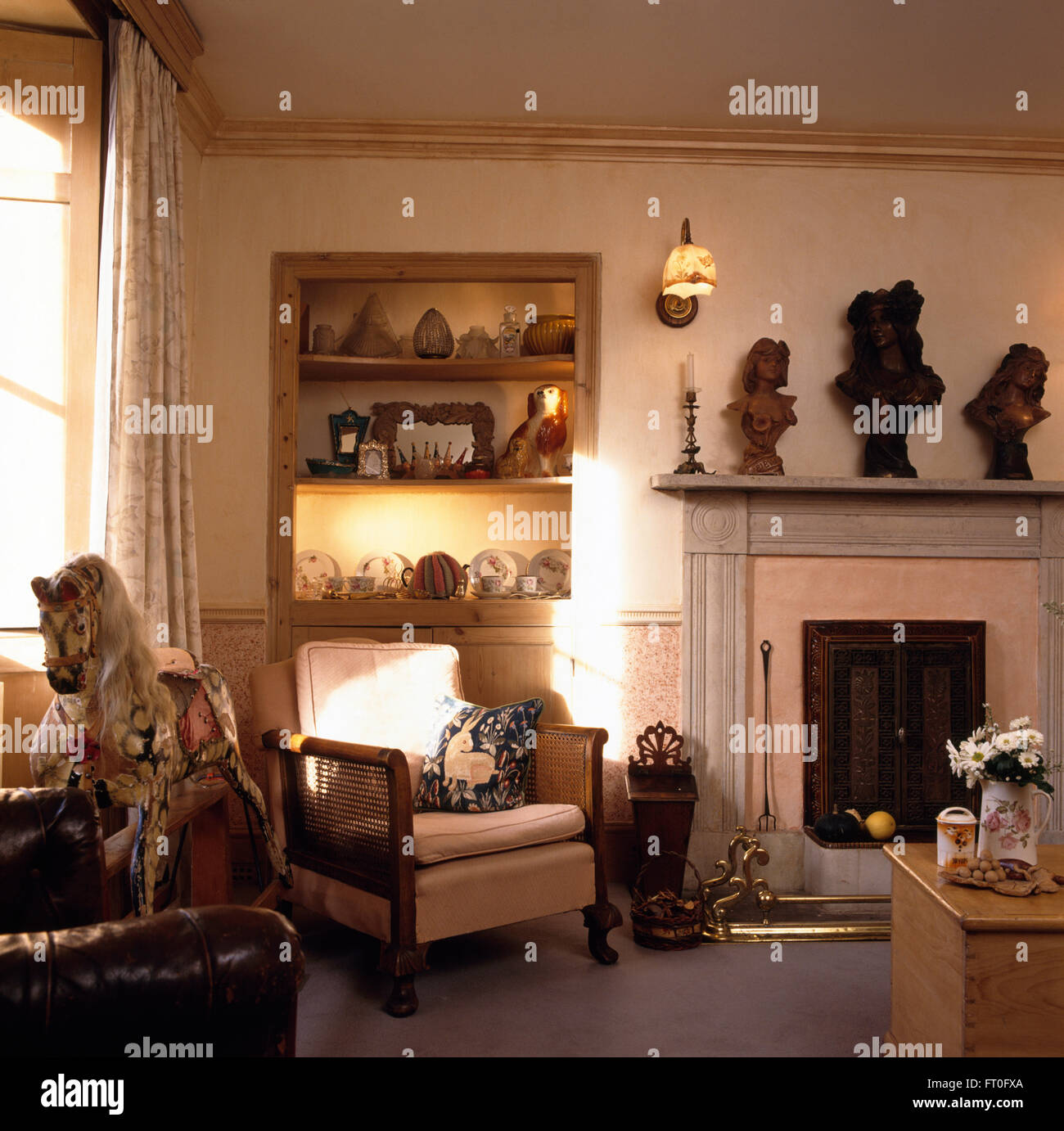 Vintage cavallo a dondolo e poltrona bergere in angolo di una crema la stanza di seduta con busti classici sul camino Foto Stock