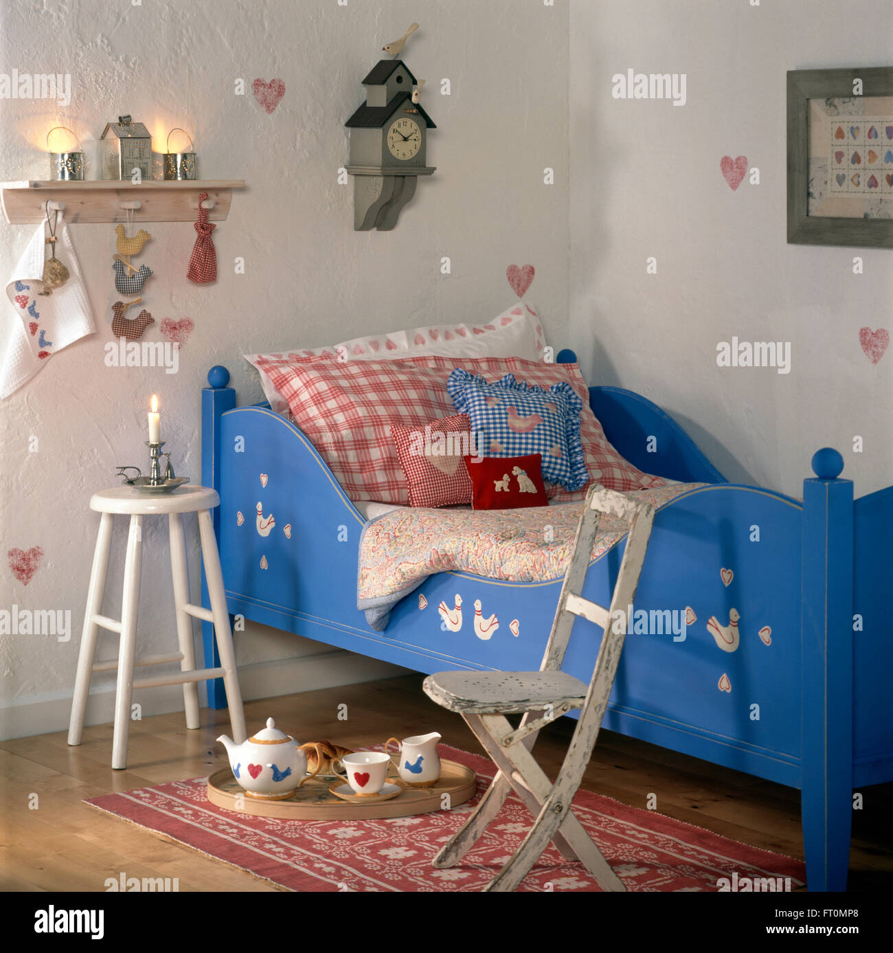 Controllare coloratissimi cuscini su dipinto di blu letto in camera bambino con una sedia in legno e sgabello Foto Stock