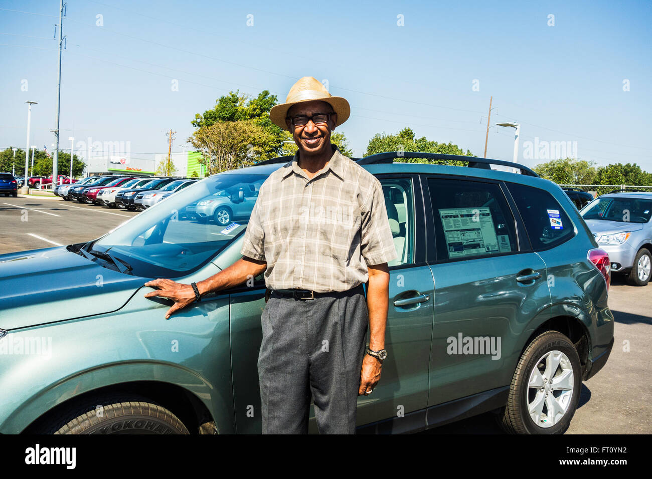 An African American automobile venditore sorge accanto a una nuova automobile per la vendita in Edmond, Oklahoma, Stati Uniti d'America. Foto Stock