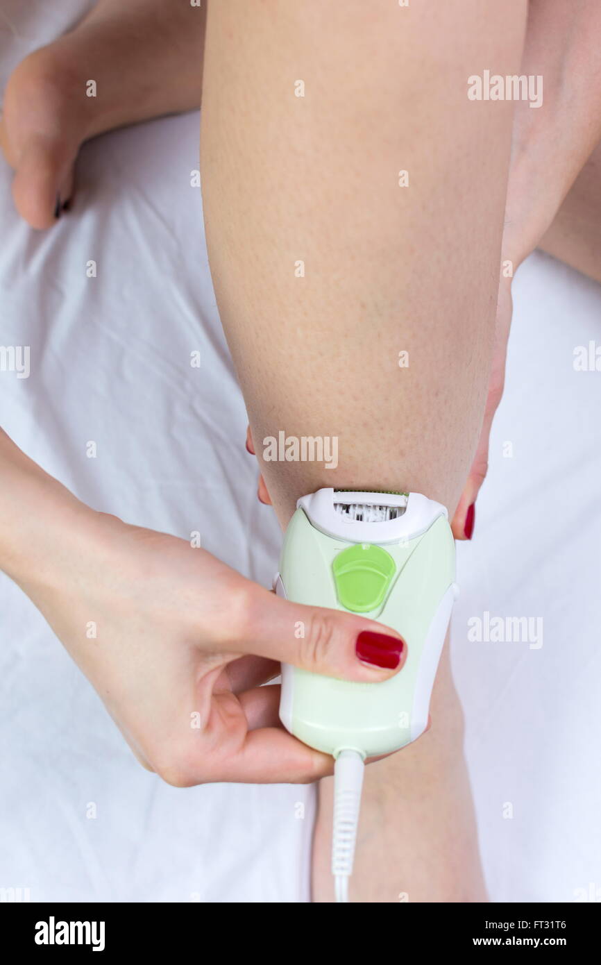 Ragazza epilates la gamba con un epilatore a casa Foto Stock