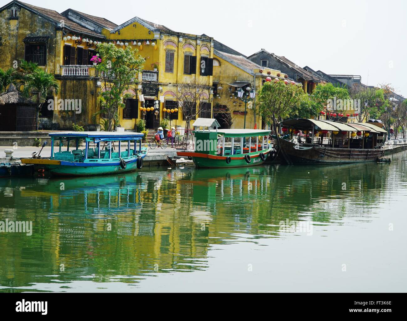 Le imbarcazioni turistiche ormeggiato sul fiume in Hoi An, Vietnam. Lo stile coloniale degli edifici lungo le strade. Foto Stock