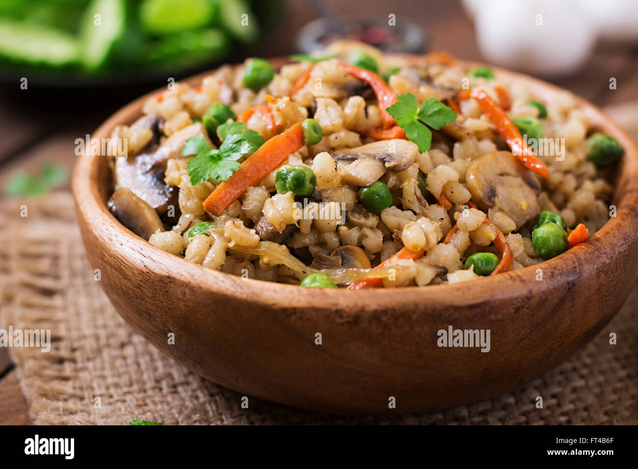 Friabile vegetariana orzo perlato porridge con funghi e piselli verdi in una ciotola di legno Foto Stock