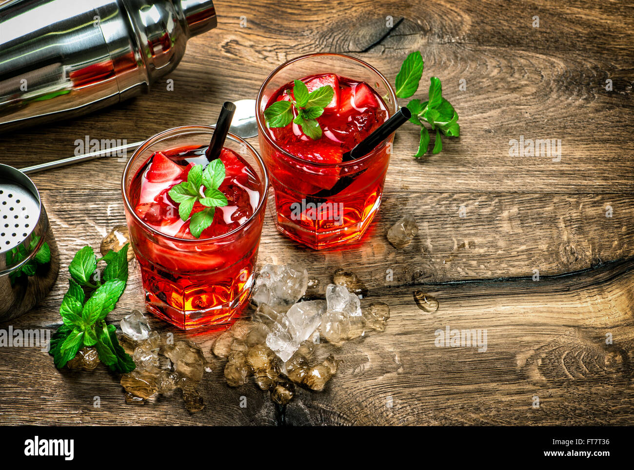 Bicchieri di rosso cocktail con ghiaccio, foglie di menta e fragola sulla cucina in legno tavolo. In stile vintage tonica foto Foto Stock