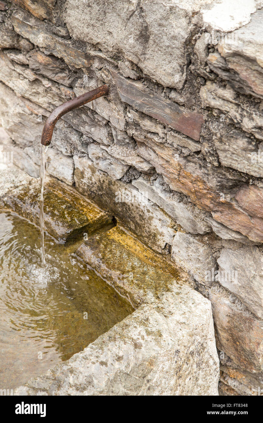 Close-up del rubinetto di ferro nel muro di pietra all'aperto con acqua che scorre nel serbatoio coperto con moss Foto Stock