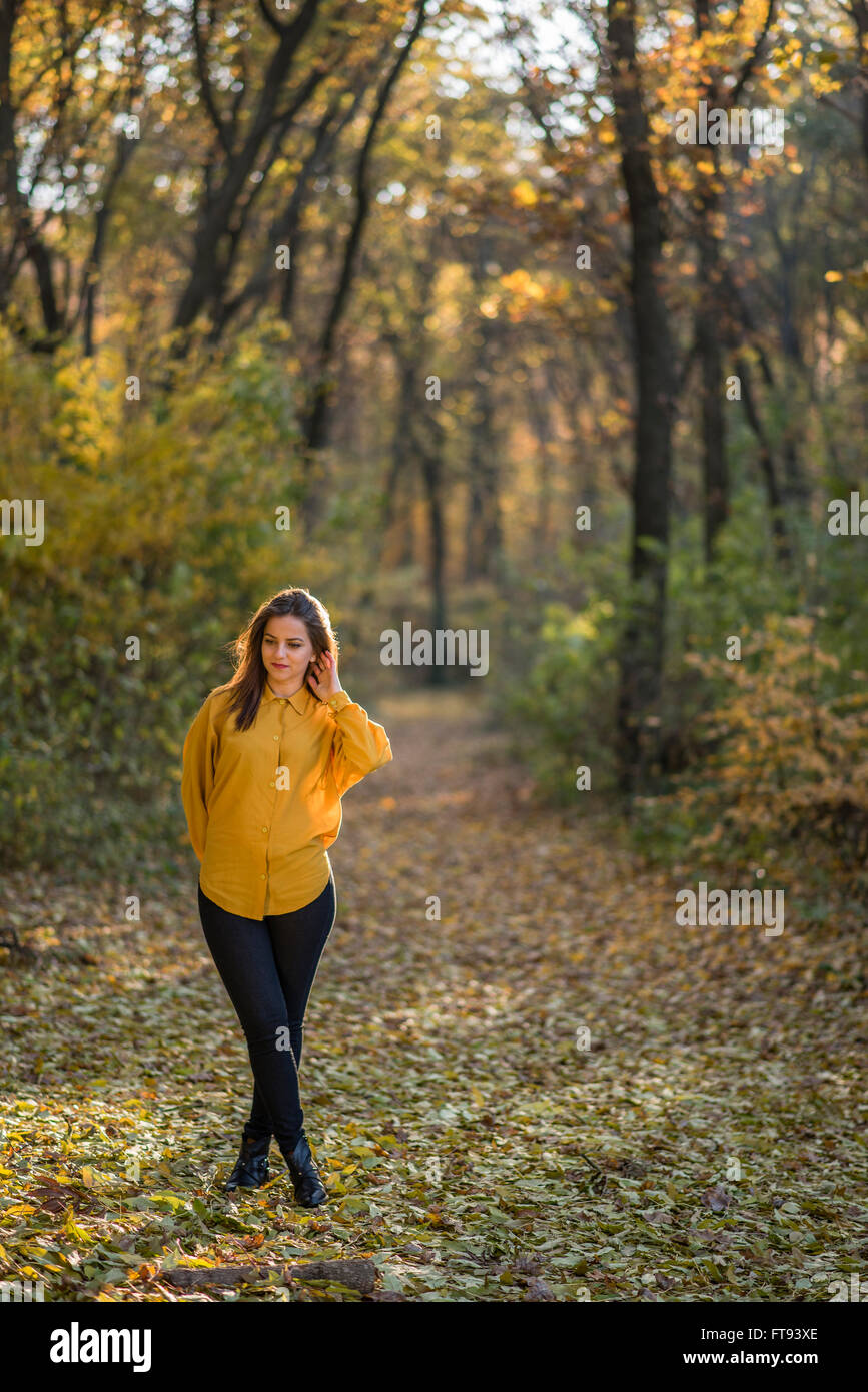 Premurosa ragazza nella foresta di autunno. Una bella ragazza in stretch jeans e maglietta gialla è in posa di una foresta. Essa non cerca Foto Stock