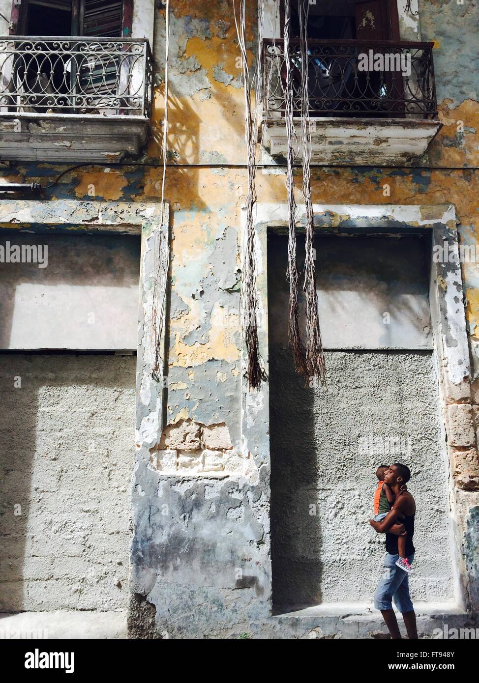 Un uomo porta un figlio passato un vecchio edificio con appeso albero radici nella vecchia Havana, Cuba Foto Stock