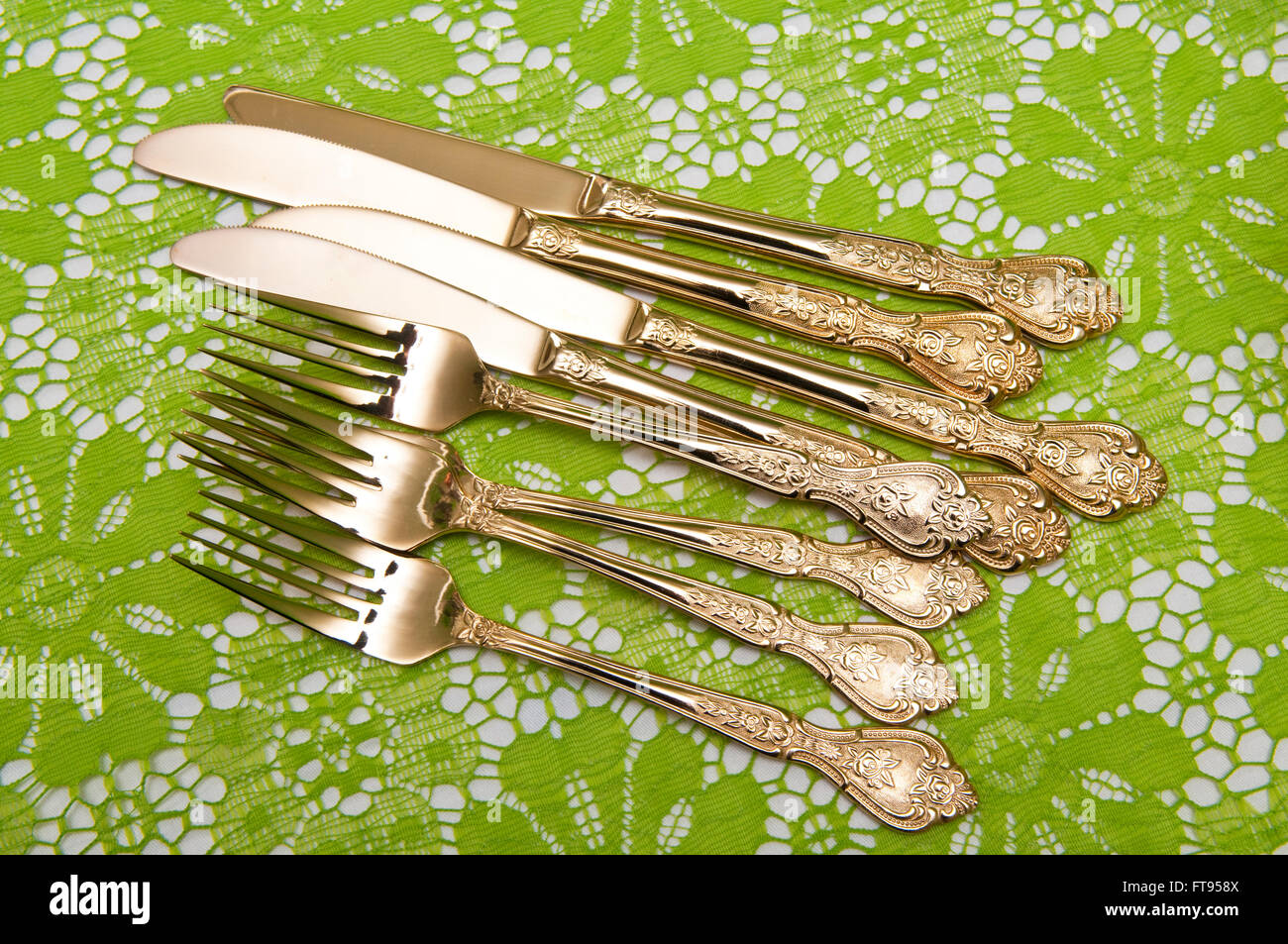 Placcato oro posate o posate su un verde tovaglia di pizzo Foto Stock
