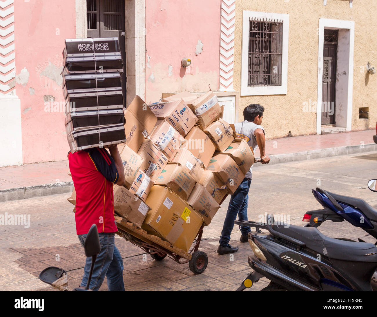 Shop le consegne. Due uomini, uno con una trazione del carrello e uno con le scatole di scarpe impilati a piedi la strada di ciottoli di consegnare la merce Foto Stock