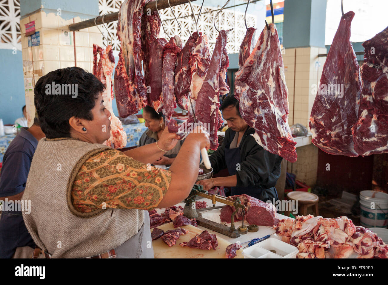 Rendendo cottura carni bovine sul mercato. Una donna del macellaio fette una striscia di carni bovine provenienti da un grande appeso pezzo di carne di manzo. Foto Stock