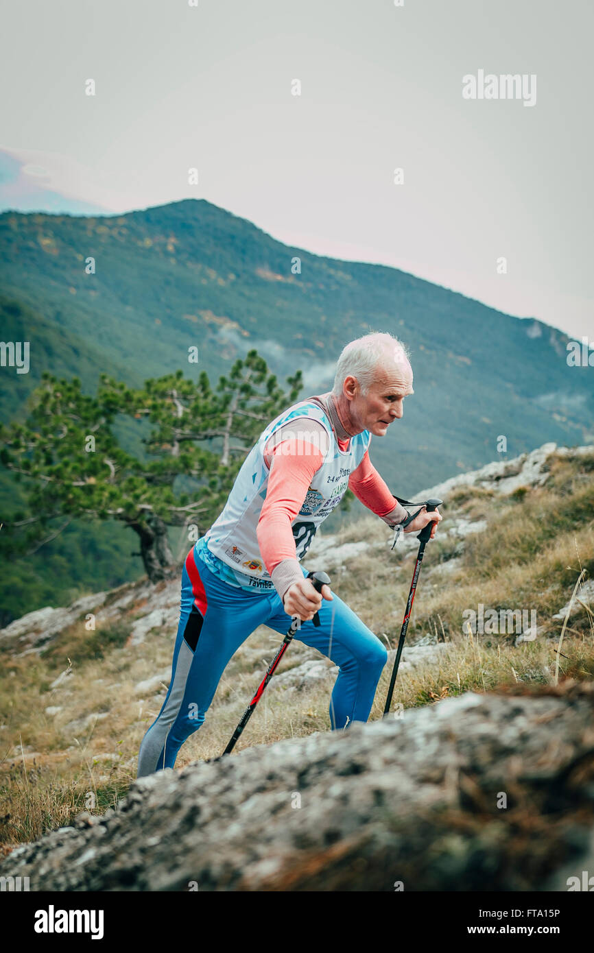 Atleta maschio senior anni con bastoni da passeggio in salita durante la maratona di montagna Foto Stock