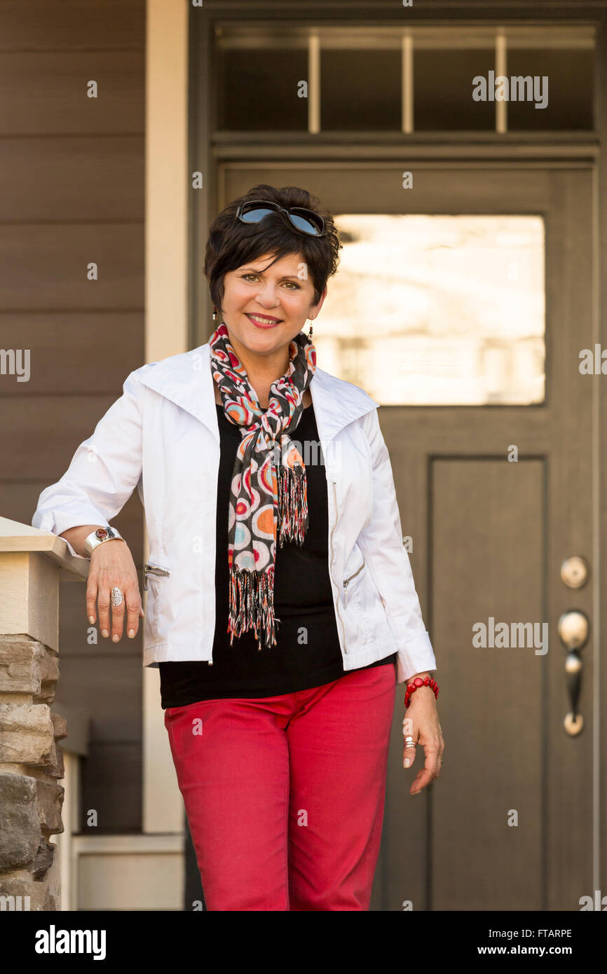 Felice, fiducioso, maturo, di mezza età della donna in piedi di fronte a una casa. Lei potrebbe essere il proprietario di casa o di un agente immobiliare. Foto Stock