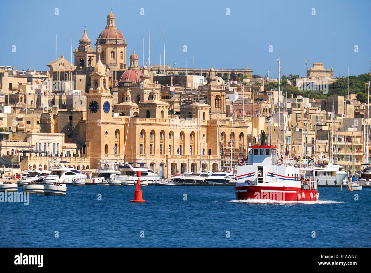 La vista di edifici storici di Birgu attraverso il Dockyard Creek con crociere nave passando lungo la costa di Malta. Foto Stock