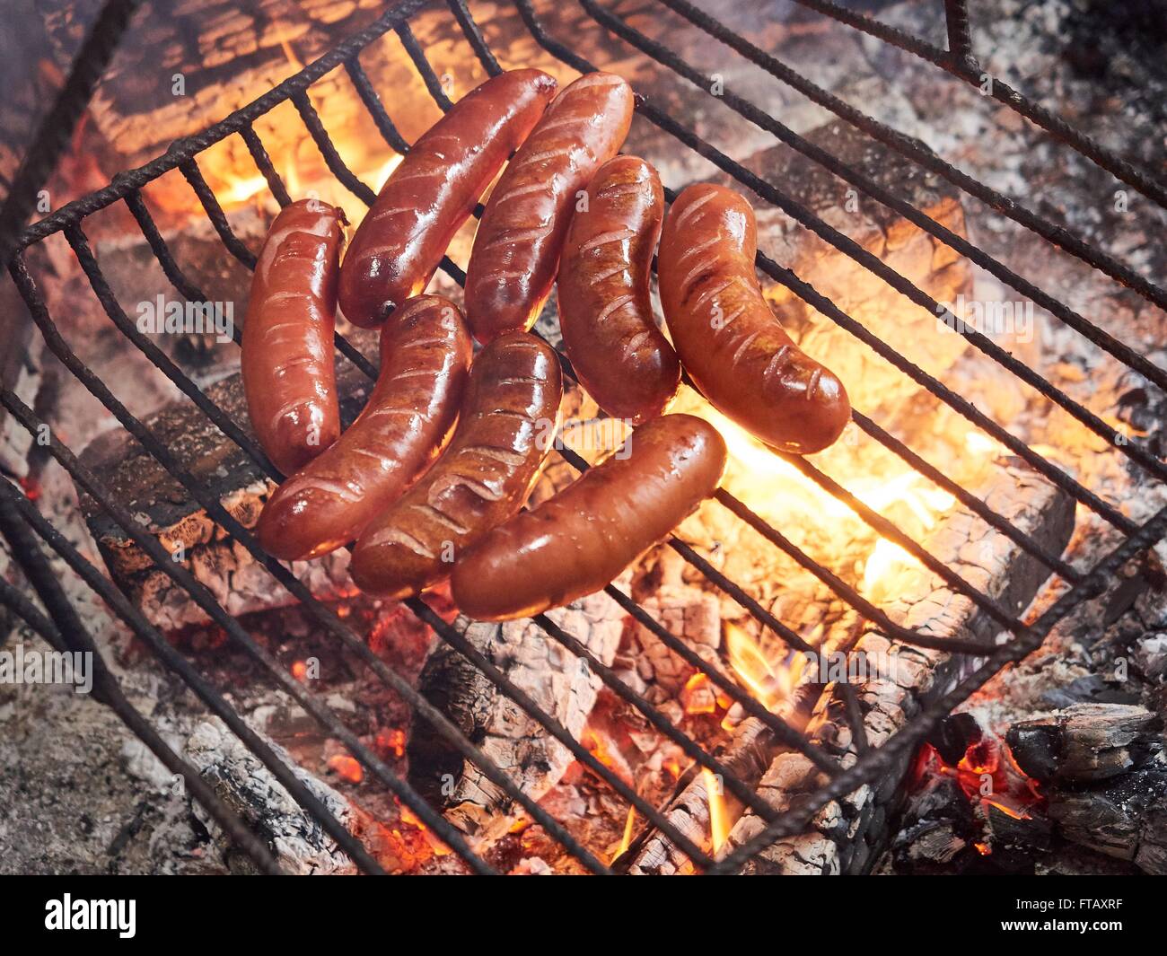 Salsicce in grill all'aperto. Primo piano immagine di malsana ma il cibo è delizioso e fiamme di fuoco. Foto Stock