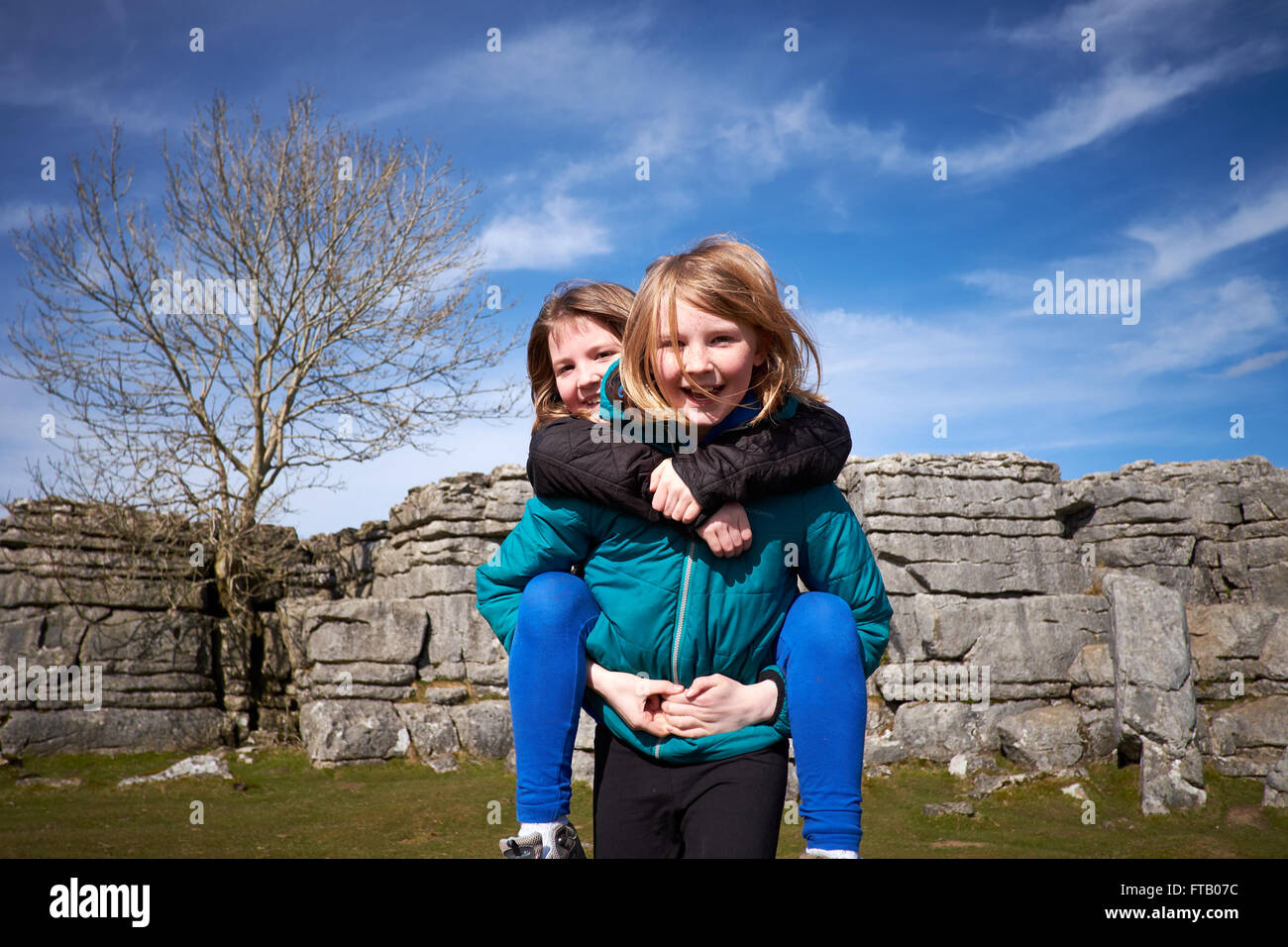 Due ragazze, sorelle, di fronte a una formazione di calcare e il cielo blu, dando un piggy-back e sorridente alla fotocamera. Foto Stock