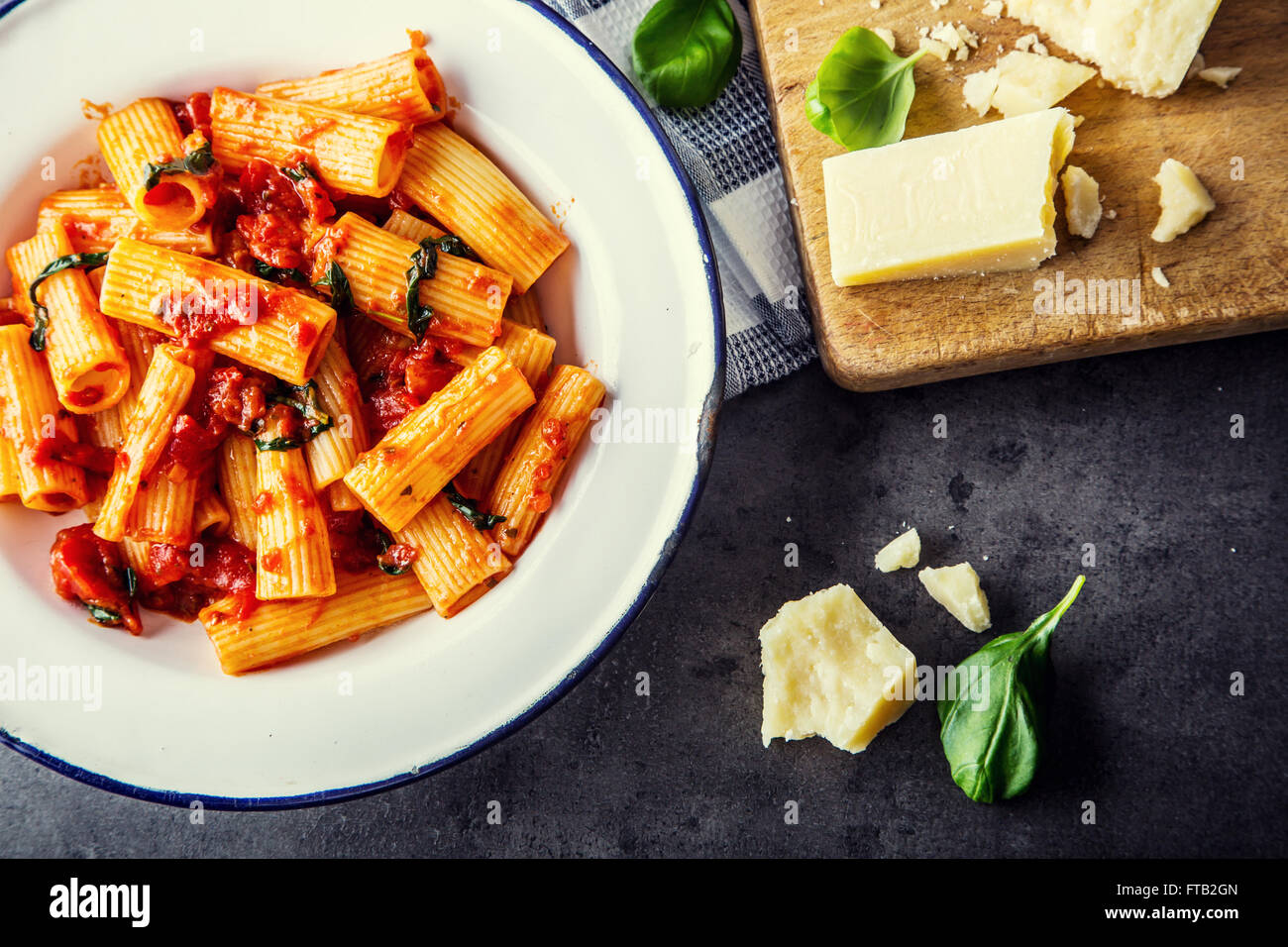 La pasta. Cucina italiana e mediterranea. Pasta Rigatoni con salsa di pomodoro foglie di basilico e aglio formaggio parmigiano. Una vecchia casa Foto Stock