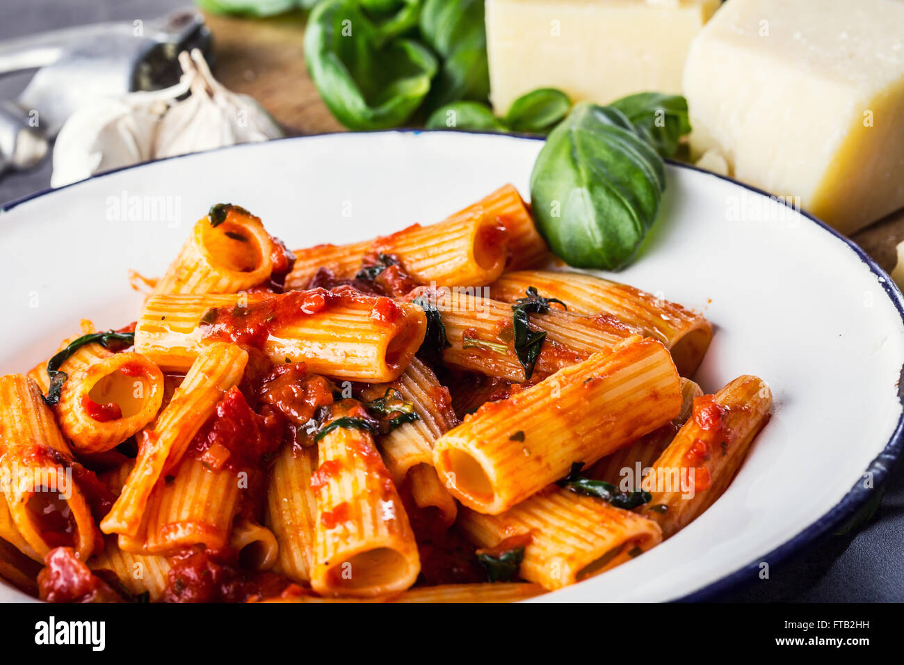 La pasta. Cucina italiana e mediterranea. Pasta Rigatoni con salsa di pomodoro foglie di basilico e aglio formaggio parmigiano. Una vecchia casa Foto Stock