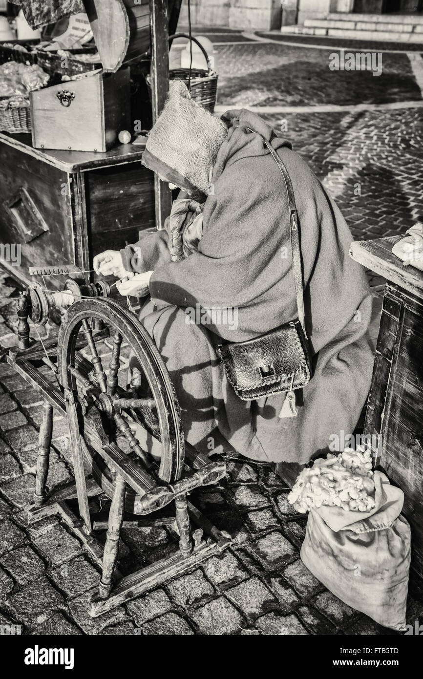 Donna anziana utilizza i bozzoli di bachi da seta a girare utilizzando una vecchia ruota di filatura di legno. Foto Stock