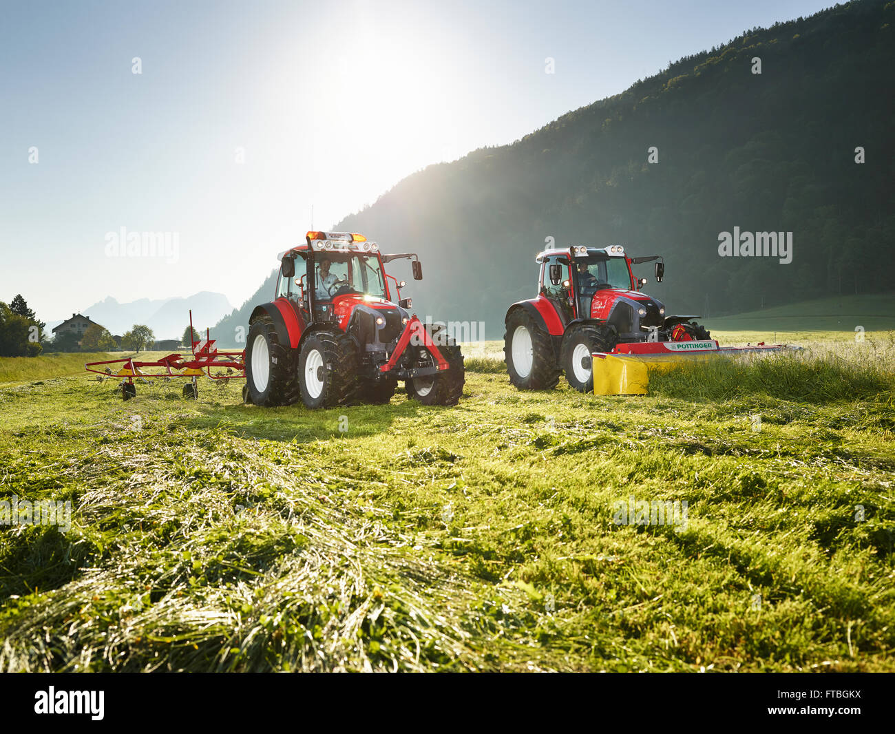 Due trattori sfalcio e spandimento del fieno il fieno tagliato, Kundl, Valle Inn, Tirolo, Austria Foto Stock
