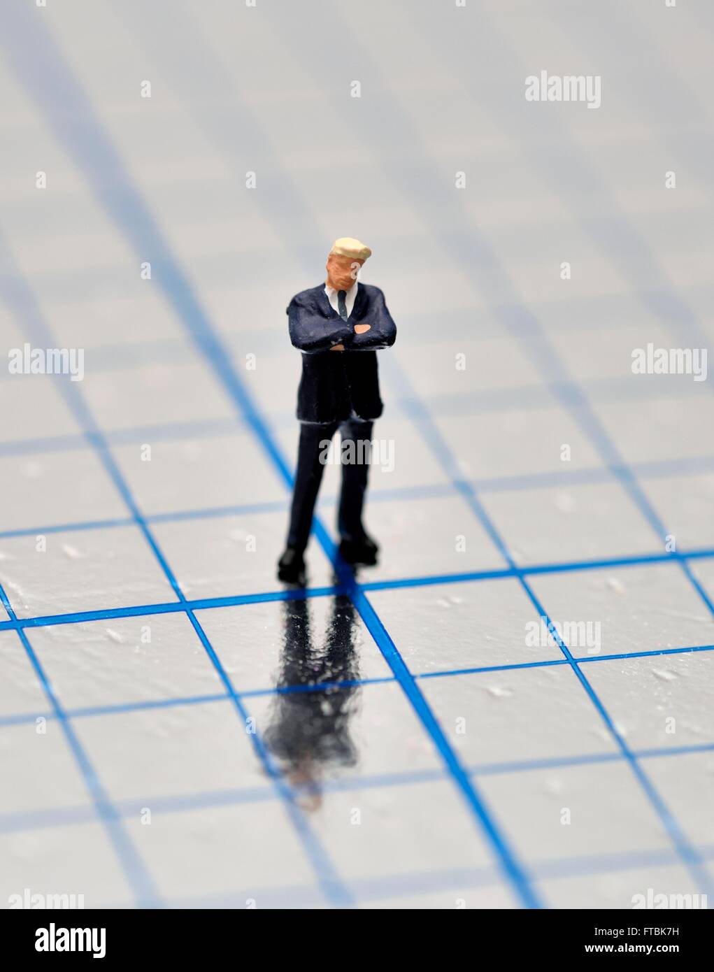 Statuetta in miniatura imprenditore con le braccia incrociate in piedi su un quadrato blu superficie lucida. Foto Stock